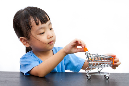 Chinese little girl pushing a toy shopping cart in plain white isolated background.