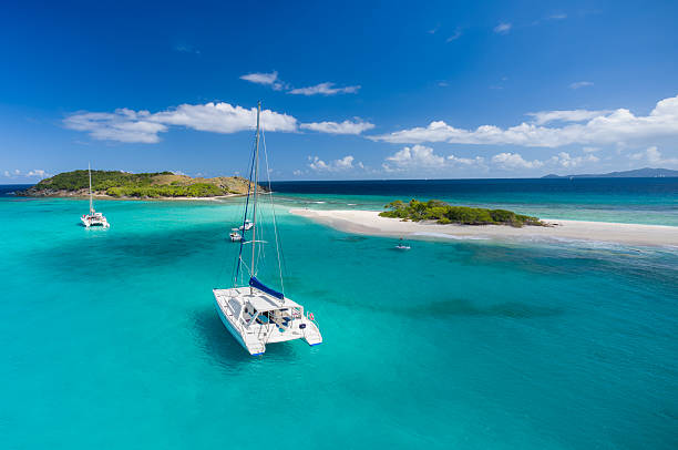 Catamaran at anchor in front of deserted island Aerial view of a catamaran at anchor in front of Sandy Spit, British Virgin Islands, Caribbean cay photos stock pictures, royalty-free photos & images