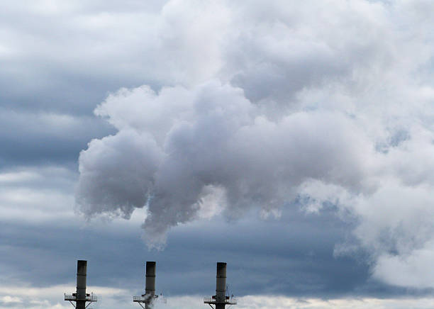 Three Billowing Industry Smoke Steam Stacks Environment Pollution Health Three industrial steam chimneys with billowing smoke on a blue cloudy sky.  The industry stacks are a concern of environmental pollution. air quality stock pictures, royalty-free photos & images