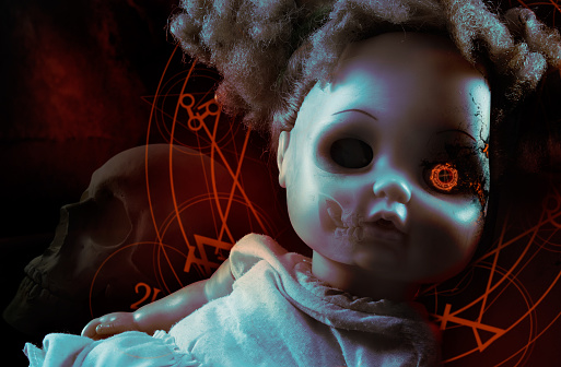 Possessed demonic horror doll with red pentacles, glowing eye & human skull on background.