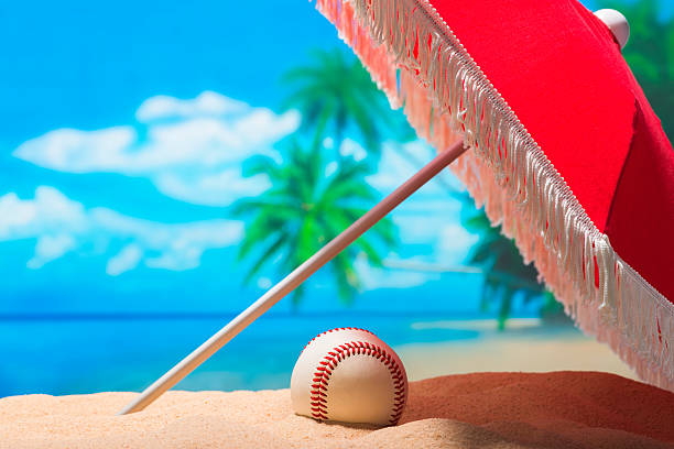 Baseball on the beach for Spring Training Grapefruit League A baseball sitting under a red umbrella with white fringe on the beach for the Grapefruit League in Fllorida for Spring Training, with palm trees and ocean in the background baseball baseballs spring training professional sport stock pictures, royalty-free photos & images