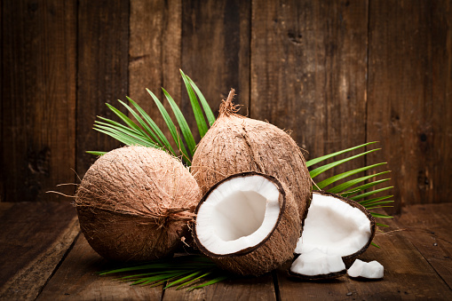 Two whole coconuts, an open coconut and coconut pieces shot on rustic wood table. DSRL studio photo taken with Canon EOS 5D Mk II and Canon EF 100mm f/2.8L Macro IS USM