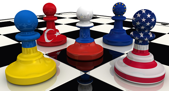 Chess pieces on the board - the pawn in the colors of the Russian flag surrounded by the pawns in colors of the flags of the United States, Ukraine, EU, Turkey. The concept of the siege (blockade) of the Russian Federation. The three-dimensional illustration. Isolated