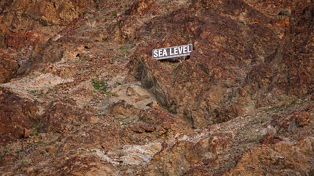 Sea Level Sign on Mountain Side in Death Valley Looking up to view sea level sign on mountain side at Badwater Basin in Death Valley National Park view into land stock pictures, royalty-free photos & images