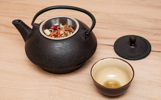 Angled view of a metal black asian style teapot and tea up on a wooden table