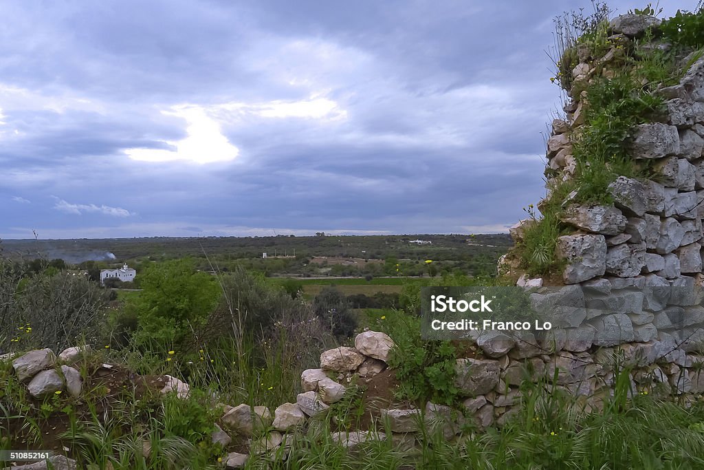 Agricultural landscape. Ruins ancient wall up the hill,fields cultivated and farms to valley and cloudy sky above the scene. Agricultural Activity Stock Photo