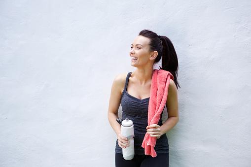 Portrait of a smiling sporty woman standing with water bottle and towel