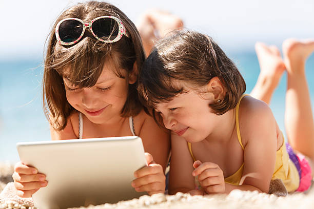 сестры, используя планшетный компьютер на пляже - child beach digital tablet outdoors стоковые фото и изображения