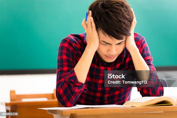 Stressed Student Studying For Exam In Classroom Stock Photo - Download Image Now - Teenager, Headache, Student