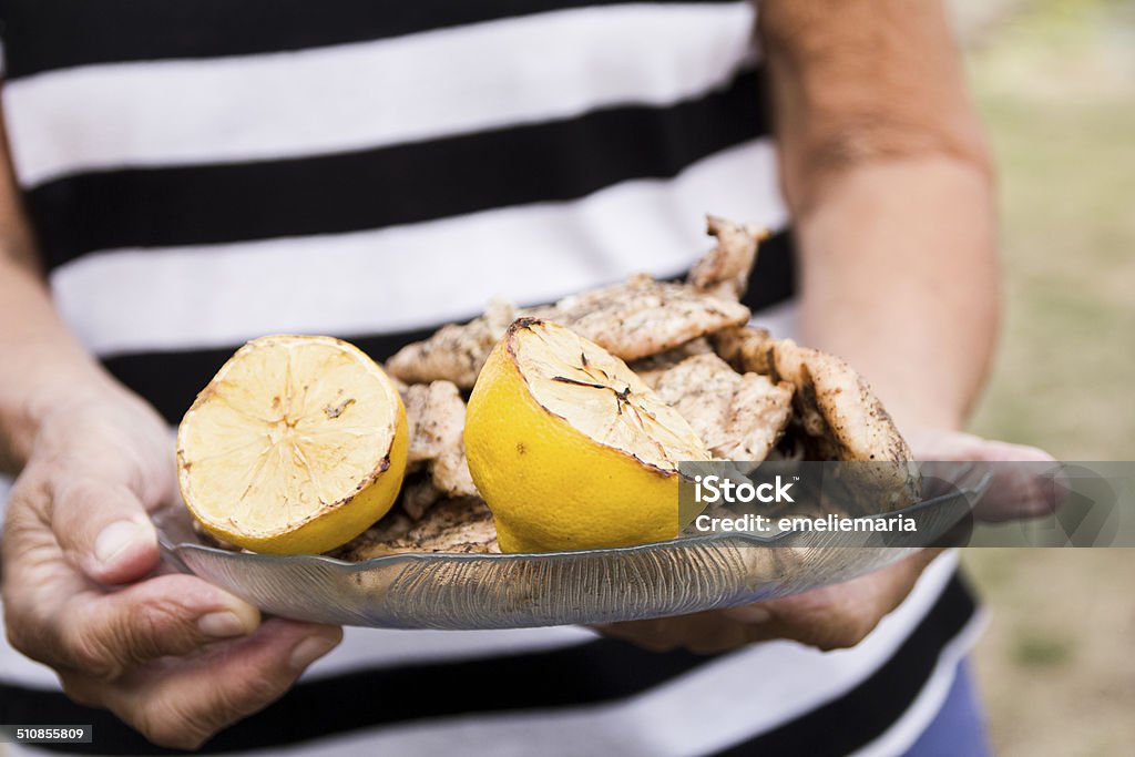 Female hands holding plate with fresh grilled food Female hands holding a plate with grilled chicken and lemon on an outside family dinner in summer symbolizing fresh, healthy summer food and happy family times. Multicolored image.  Adult Stock Photo