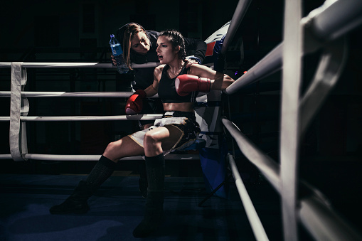 Photo of a female boxer sitting in a boxing ring corner.  She is listening to advices from her trainer.