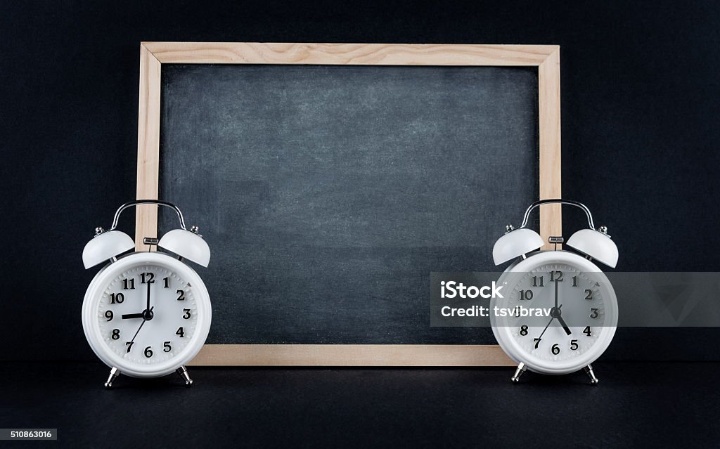 Nine to 5 corporate working hours concept Two vintage alarm clocks showing 9 and 5 o'clock with empty chalkboard on black background. Nine to five corporate working hours concept. 5 O'Clock Stock Photo