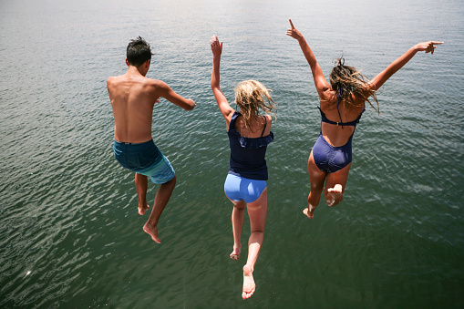 Young traveler jumps against backdrop of forest and lake raising hands to sky. Active and healthy lifestyle and travel