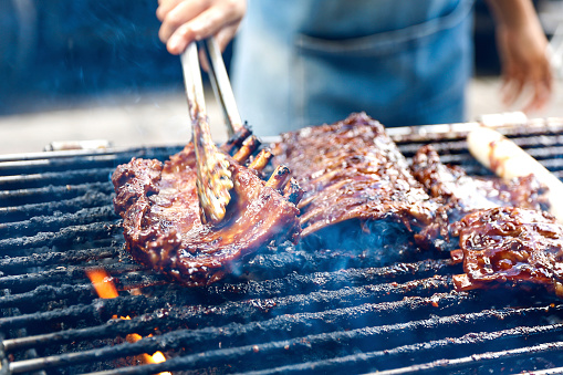 Barbecue pork ribs-grilled. A close up photo of a chef hands grilled a barbeque pork ribs. The chef holding the ribs with a tongs. For more pictures like this https://secure.istockphoto.com/search/lightbox/15915184#14248356