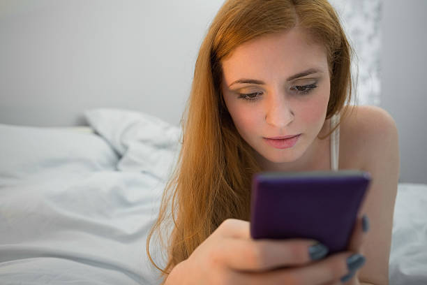 istock Happy redhead lying on bed sending a text 510869973