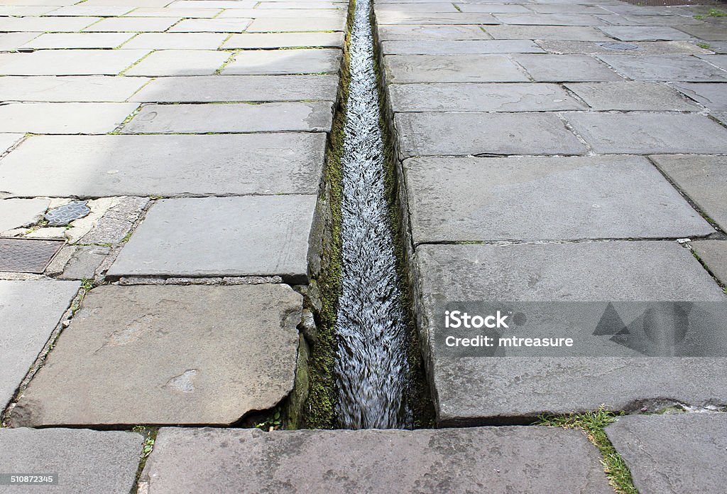 Small stream / rill running down centre of flagstone paved street Photo showing a small stream / rill running down the very centre of a shopping street with flagstone paving.   This unusual stream is to be found in the heart of Frome, a small market town in Somerset, England, UK.  The street is called Cheap Street and it dates back many centuries. Frome Stock Photo