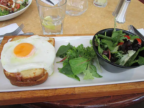 Photo showing a lunchtime meal served at a French restaurant, served on a long, rectangular white plate.  The lunch consisted of a fried smoked ham and melted Gruyere cheese, which was topped with a rather greasy fried egg and served with a small salad (green lettuce leaves and beetroot leaves).