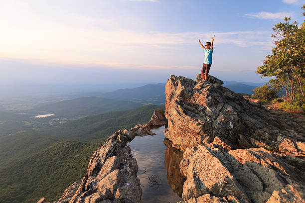 Teenager on the edge of a cliff A teenager stands on the top the Little Stony Man mountain waiting for sunset in the Shenandoah National Park shenandoah national park stock pictures, royalty-free photos & images