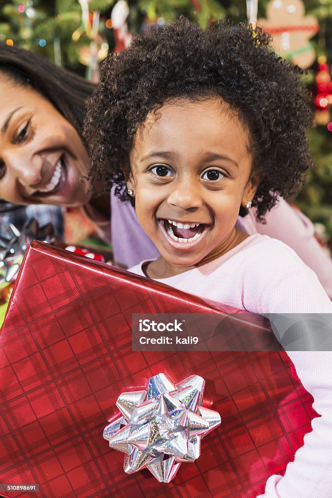 Little African American girl holding Christmas present African American little girl (5 years) holding Christmas gift, excited over Christmas gift, grinning at camera.  Proud mother laughing.  Focus on daughter. Single Mother Stock Photo