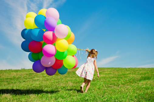 Happy little girl holding colorful balloons. Child playing on a green meadow. Smiling  kid.