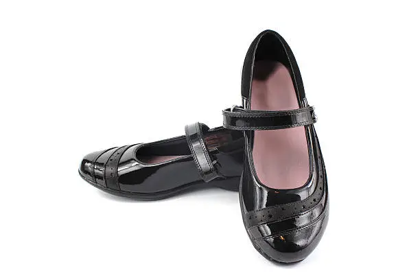 Girl's shiny black patent leather shoes on white background.
