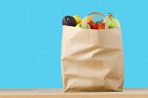 Fruit Shopping Bag A brown paper shopping bag, filled to the top with varieties of fruit, on a light wood surface.  Isolated on a turquoise blue background. handle photos stock pictures, royalty-free photos & images
