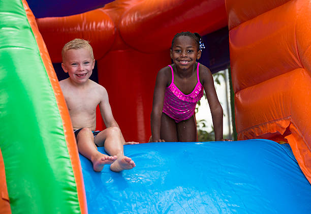 feliz niños deslizante de una casa de rebote colchonetas inflables - inflatable child playground leisure games fotografías e imágenes de stock