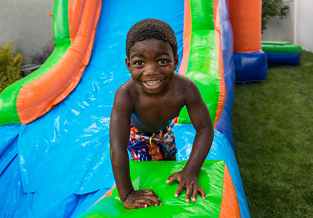 uśmiechająca się mały chłopiec przesuwne w dół na nadmuchiwane bounce dom - inflatable slide sliding child zdjęcia i obrazy z banku zdjęć