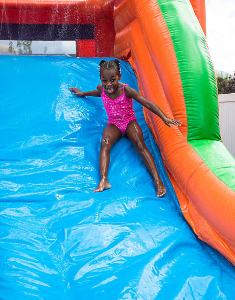 sorridente menina jogando no slide ao ar livre salto assembleia insufláveis - house bouncing multi colored outdoors imagens e fotografias de stock