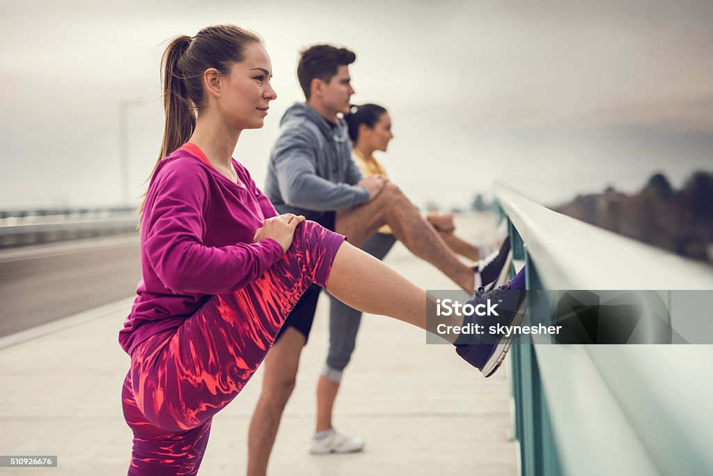 Young athletes stretching their legs outdoors before exercising. Team of young athletic people warming up and stretching their legs outdoors. Focus is on foreground, on a young woman. Sport Stock Photo