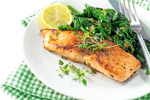 grilled salmon with thyme, lemon and spinach on a plate, vegetarian low carb dish, green white napkin on a white background, selected focus, narrow depth of field