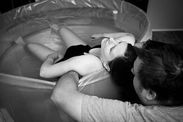 Husband Supporting Wife During Home Water Birth Black and white image of a loving husband supporting and coaching his wife through an intense home birth. water birth photos stock pictures, royalty-free photos & images