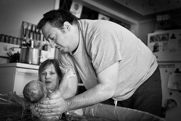 Husband Lifting Newborn From Water After Home Birth