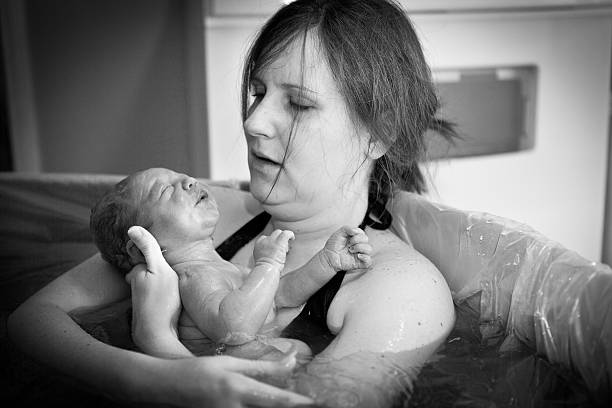 Mother Holding Newborn After Home Water Birth Black and white image of a young mother holding her newborn son after giving birth at home. water birth stock pictures, royalty-free photos & images