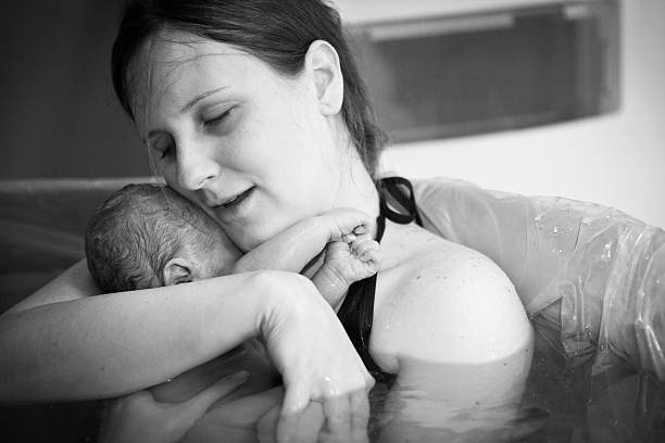 Mother Embracing Her Newborn after Home Water Birth Black and white image of a young mother embracing her newborn son after giving birth at home. water birth photos stock pictures, royalty-free photos & images