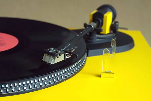 Turntable in yellow case playing a vinyl record with red label. Horizontal photo top view closeup