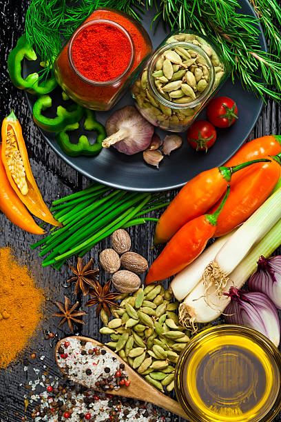 Color image depicting an overhead view of a large arrangement of fresh herbs and spices on a rustic surface. Some of the spices are contained in small ramekins, while others are on vintage spoons. The herbs and spices include paprika, coriander seeds, cumin, turmeric, basil, star anise, oregano and thyme. Plenty of room for copy space.