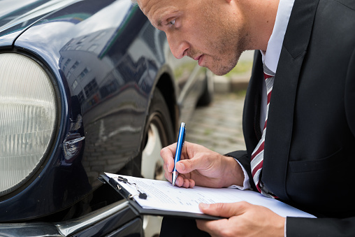 Close-up Of A Man Filling Insurance Form Near Damaged Car