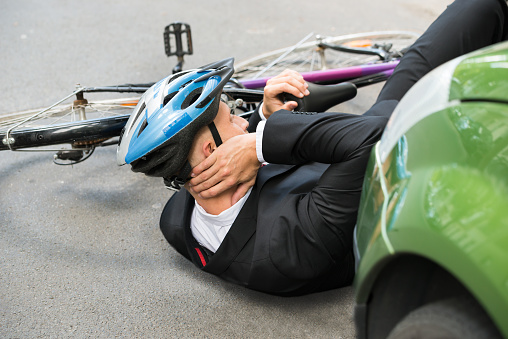 Male Cyclist With Neck Pain Lying On Street After Road Accident