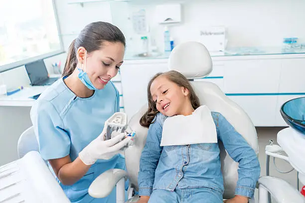 Beautiful girl at the dentist learning how to brush her teeth on a denture