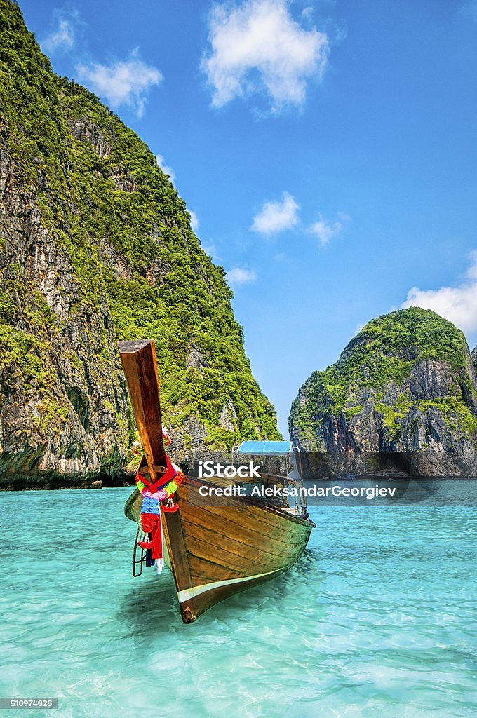 Longtail Wooden Boat at Maya Bay, Thailand Long tail wooden boat at Maya Bay on Ko Phi Phi Le, made famous by the movie titled "The Beach". Beautiful cloudscape over the turquoise water and green rocks in Maya Bay, Phi Phi Islands, Thailand. Thailand Stock Photo