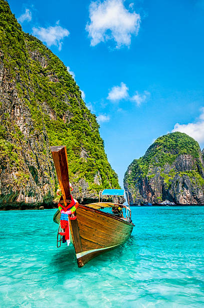 Longtail Wooden Boat at Maya Bay, Thailand Long tail wooden boat at Maya Bay on Ko Phi Phi Le, made famous by the movie titled "The Beach". Beautiful cloudscape over the turquoise water and green rocks in Maya Bay, Phi Phi Islands, Thailand. phi phi islands stock pictures, royalty-free photos & images