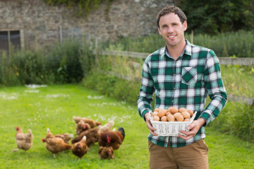 Proud young man holding a basket filled with eggs with chickens behind him