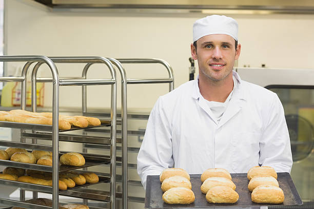 baker joven feliz sosteniendo algunas rollos en una bandeja de horno - commercial kitchen bakery front view baking fotografías e imágenes de stock