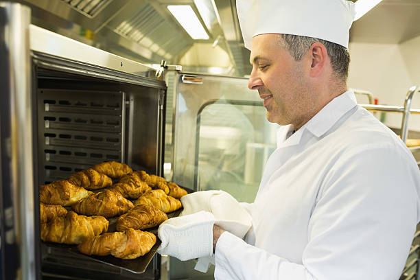 istock Mature baker putting some croissants into an oven 510995831