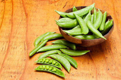 Fresh snap peas in a wooden bowl on a wooden table