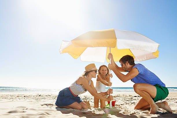 The first one to let go buys ice-cream Shot of a young family setting up an umbrella on a beach beach umbrella stock pictures, royalty-free photos & images