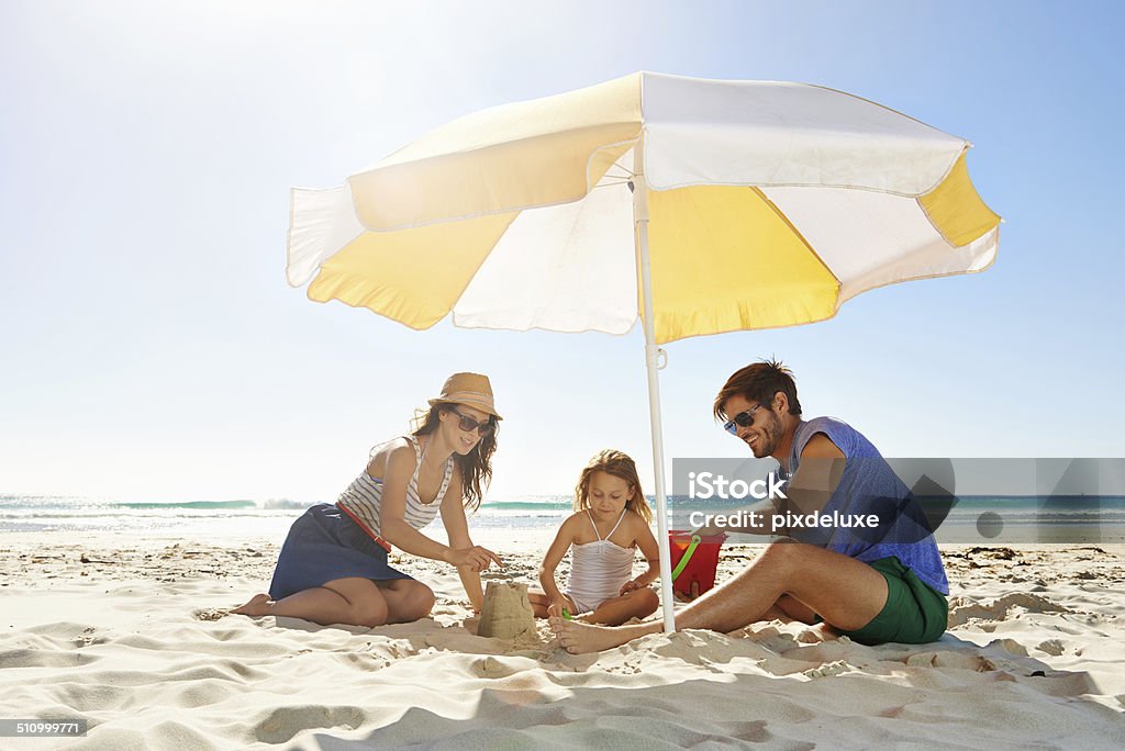 Aiutando la loro bambina costruire un castello di sabbia - Foto stock royalty-free di Famiglia