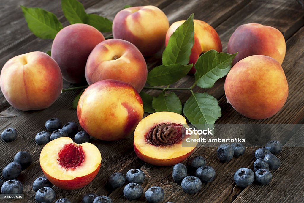 Colorful summer fruits - nectarines and peaches on wooden table Fresh Peaches and Nectarines  with green leaves on a wooden board Berry Fruit Stock Photo