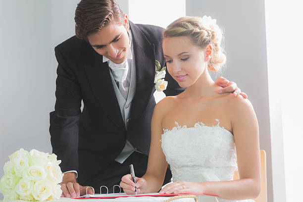 istock Young blonde bride sitting at table signing wedding register 511001239